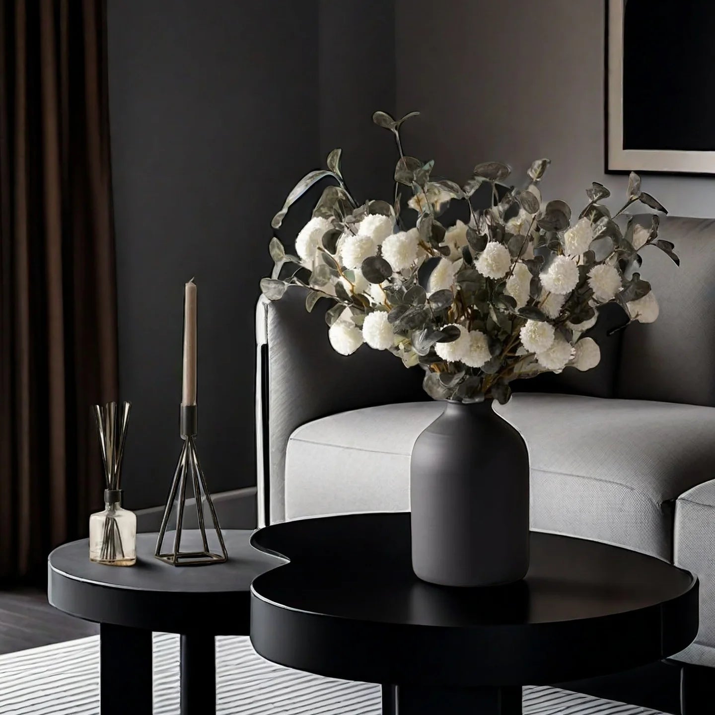 Matte black metal vase with white dried flowers on a round black coffee table in a modern living room.